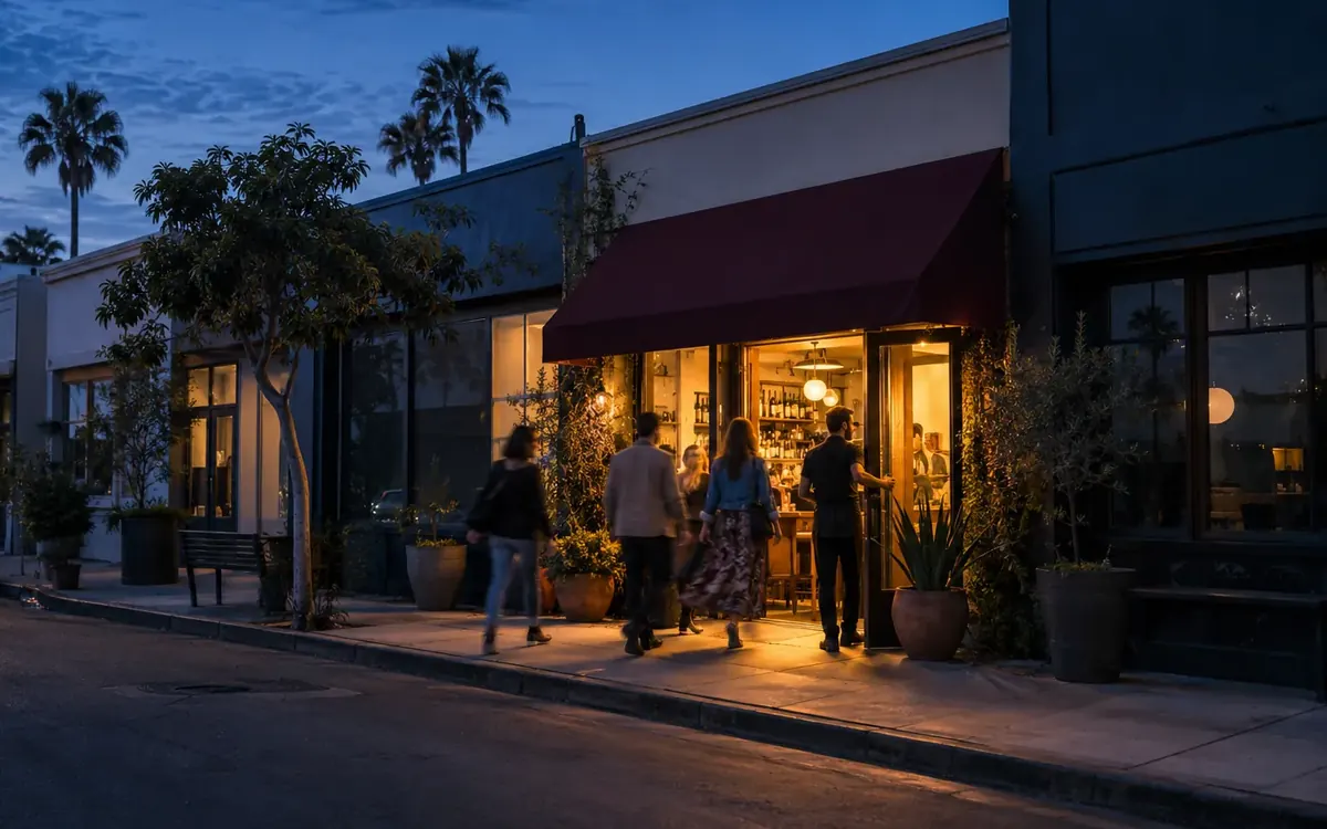 A row of shops at dusk, with customers walking into the one storefront that is lit up